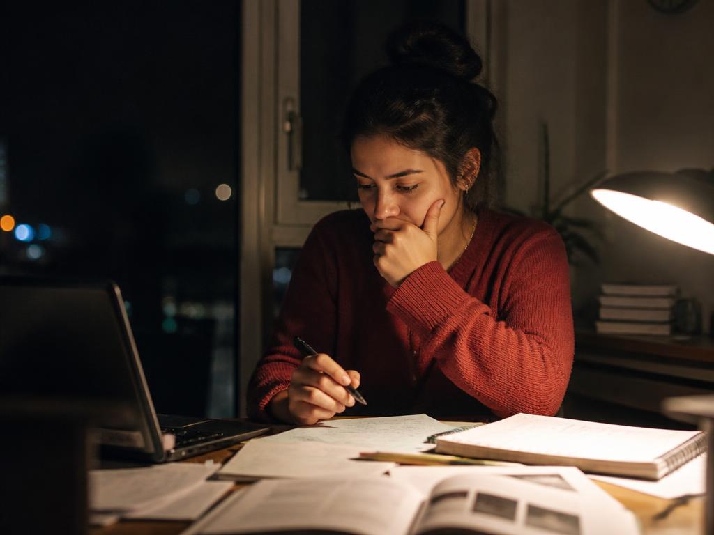 Joven estudiando de noche con gesto de autoexigencia frente a sus apuntes